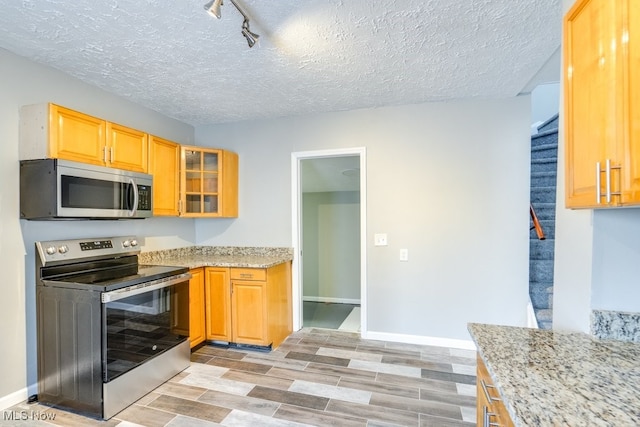 kitchen featuring glass insert cabinets, light stone counters, stainless steel appliances, a textured ceiling, and wood finish floors