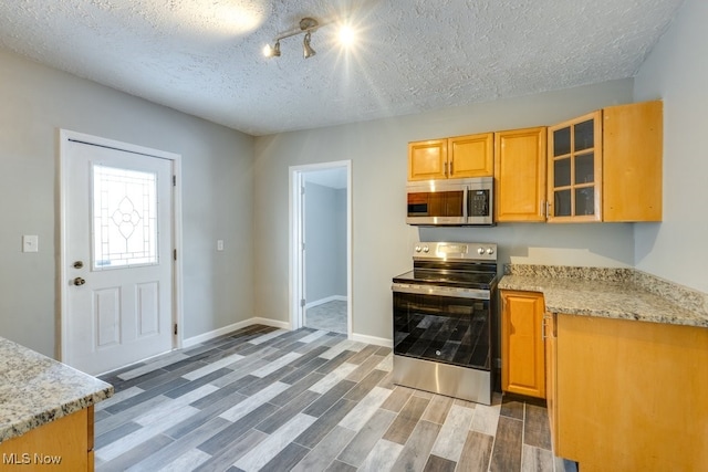 kitchen featuring baseboards, appliances with stainless steel finishes, light stone countertops, wood tiled floor, and glass insert cabinets