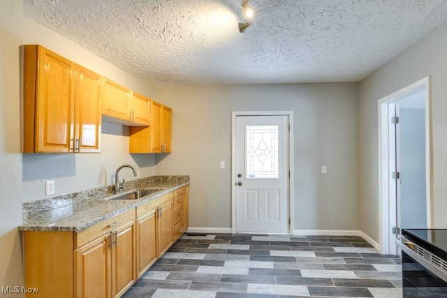 kitchen with a textured ceiling, light stone counters, wood finish floors, a sink, and baseboards