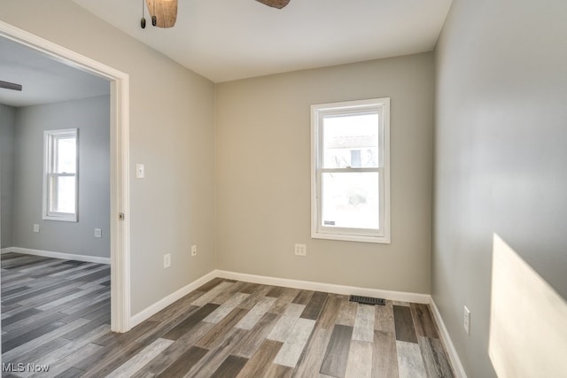 spare room with a ceiling fan, a healthy amount of sunlight, baseboards, and wood finished floors