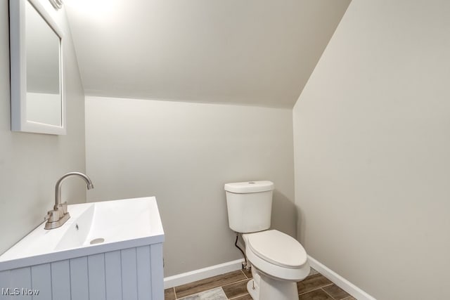 half bath featuring wood finish floors, lofted ceiling, toilet, vanity, and baseboards