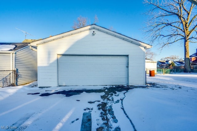 snow covered garage featuring a detached garage and fence