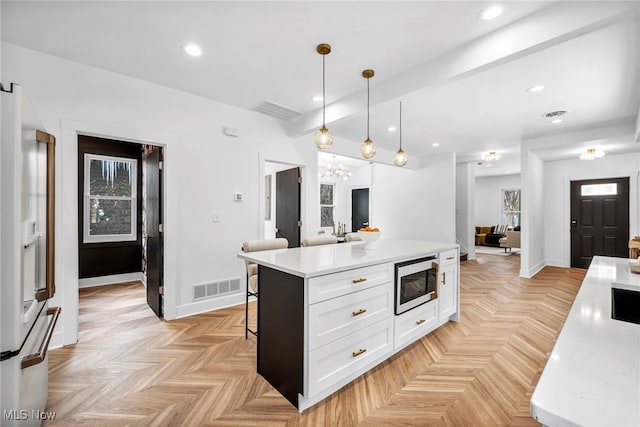 kitchen featuring a breakfast bar area, visible vents, white cabinets, built in microwave, and pendant lighting