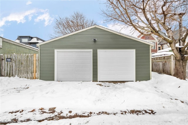 snow covered garage with a garage and fence