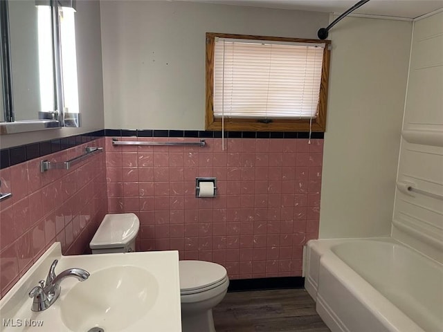 full bath featuring toilet, washtub / shower combination, a sink, and wood finished floors