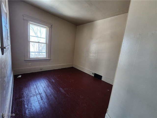 empty room featuring hardwood / wood-style flooring, visible vents, and baseboards