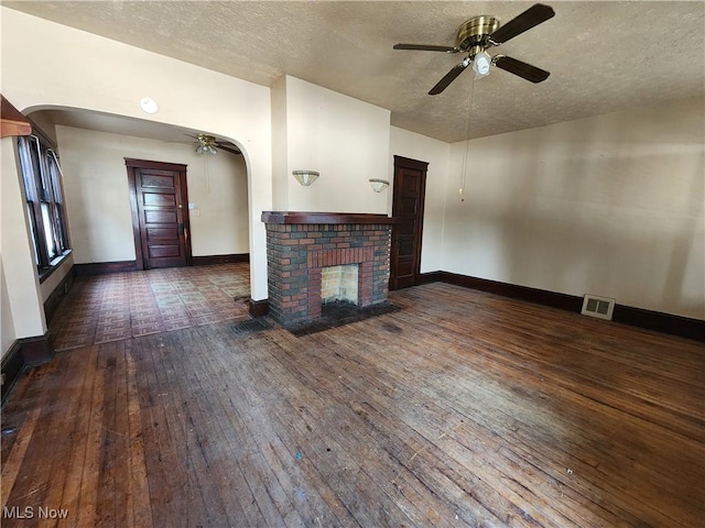 unfurnished living room with visible vents, arched walkways, baseboards, hardwood / wood-style flooring, and a fireplace