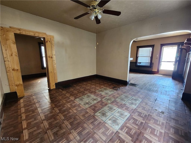 empty room with visible vents, arched walkways, ceiling fan, and baseboards