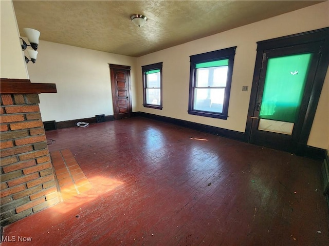 empty room featuring a textured ceiling, hardwood / wood-style flooring, and baseboards