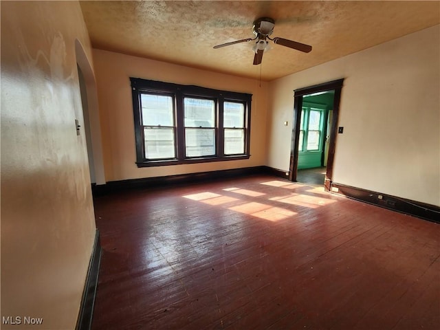 spare room featuring arched walkways, a ceiling fan, a textured ceiling, baseboards, and hardwood / wood-style flooring