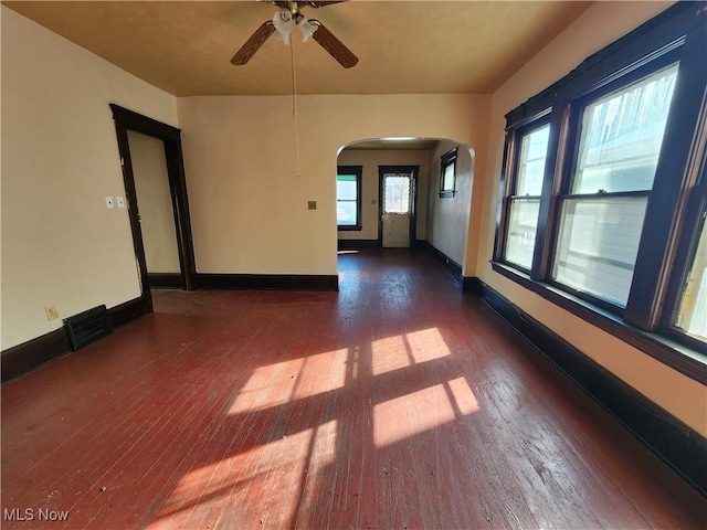 spare room featuring hardwood / wood-style flooring, visible vents, arched walkways, and baseboards