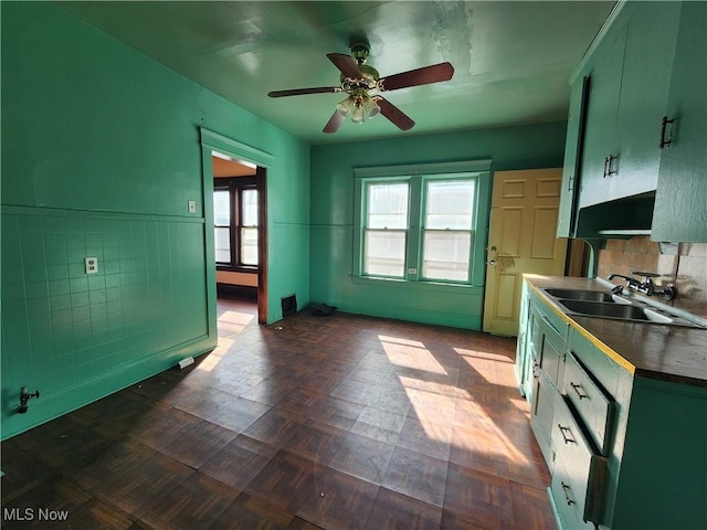 kitchen with a wainscoted wall, a sink, a ceiling fan, dark countertops, and green cabinetry