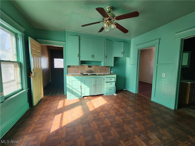 kitchen featuring wall chimney range hood, a ceiling fan, and backsplash