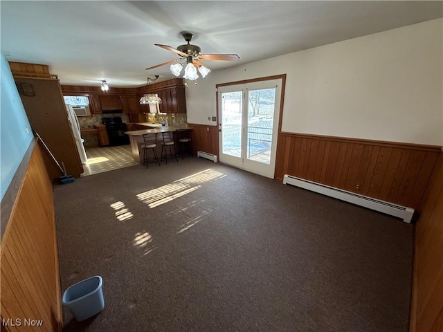 kitchen with a breakfast bar area, wainscoting, baseboard heating, and dark colored carpet