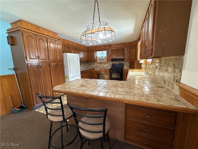 kitchen featuring tile counters, freestanding refrigerator, black gas range oven, and a peninsula