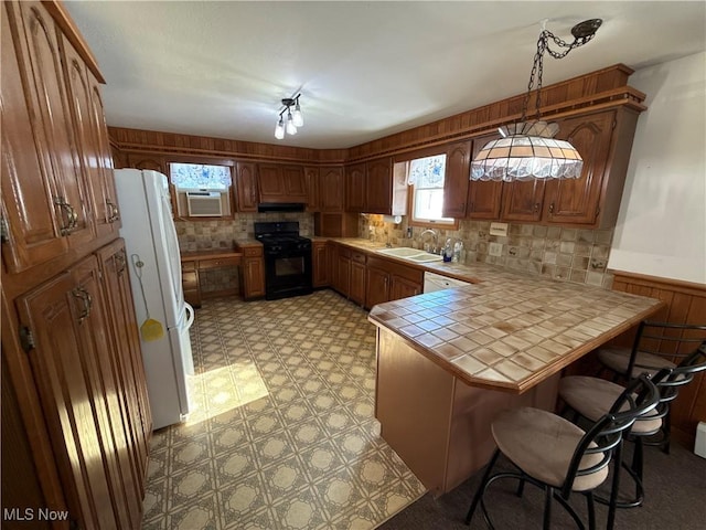 kitchen featuring a peninsula, black range oven, freestanding refrigerator, brown cabinetry, and decorative light fixtures