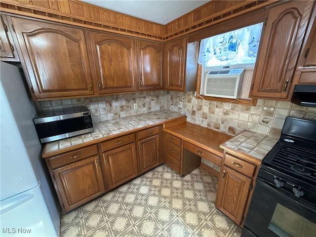 kitchen featuring freestanding refrigerator, stainless steel microwave, black range with gas cooktop, and tile counters