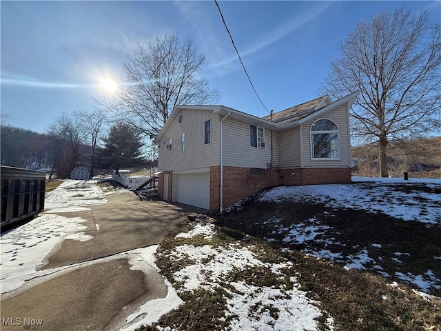 view of snow covered exterior featuring a garage, driveway, and brick siding