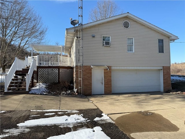 view of snow covered exterior featuring driveway, an attached garage, stairs, and brick siding