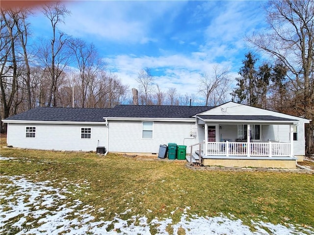 snow covered rear of property featuring covered porch, a shingled roof, and a yard