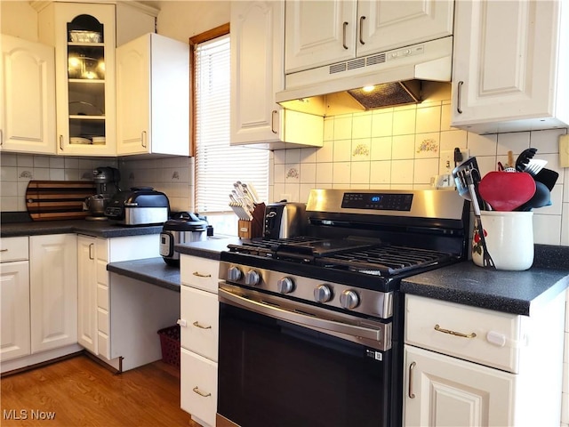 kitchen featuring stainless steel gas range, dark countertops, glass insert cabinets, and under cabinet range hood