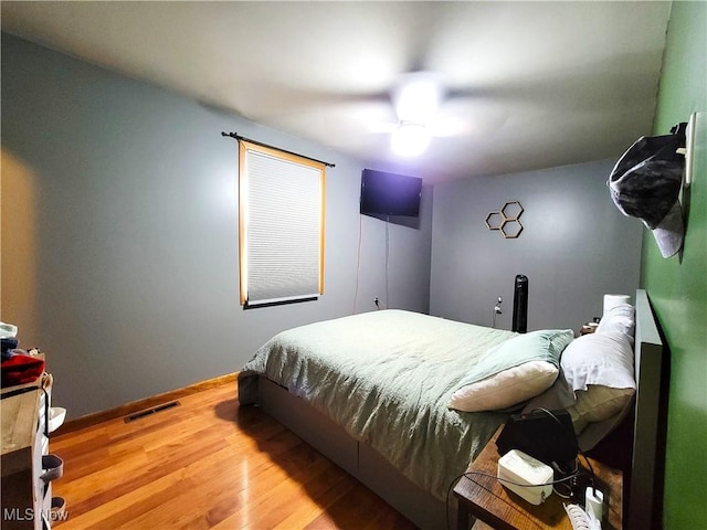 bedroom with a ceiling fan, visible vents, baseboards, and wood finished floors