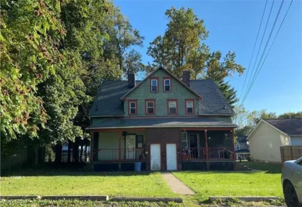 view of front of property with covered porch, a chimney, and a front yard