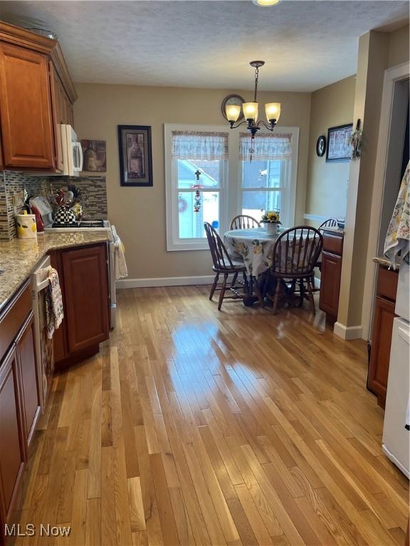 kitchen with light wood finished floors, white microwave, decorative light fixtures, light stone countertops, and backsplash