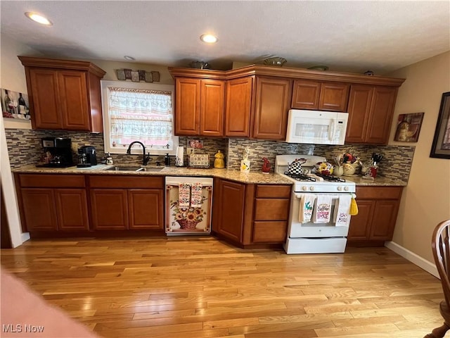 kitchen with white appliances, brown cabinets, a sink, and light wood-style flooring