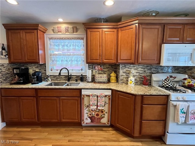 kitchen with white appliances, a sink, light stone countertops, and light wood-style floors