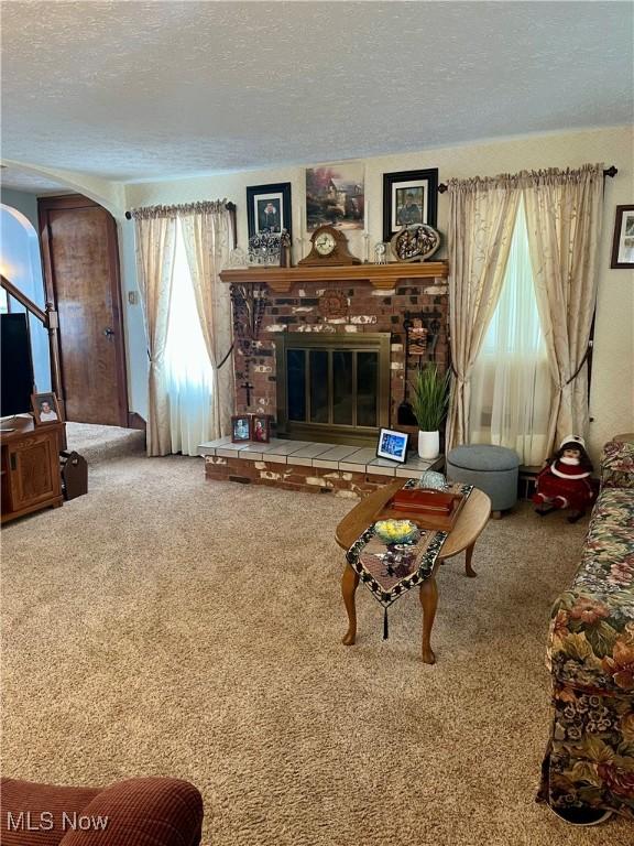 living area featuring arched walkways, carpet flooring, a fireplace, and a textured ceiling