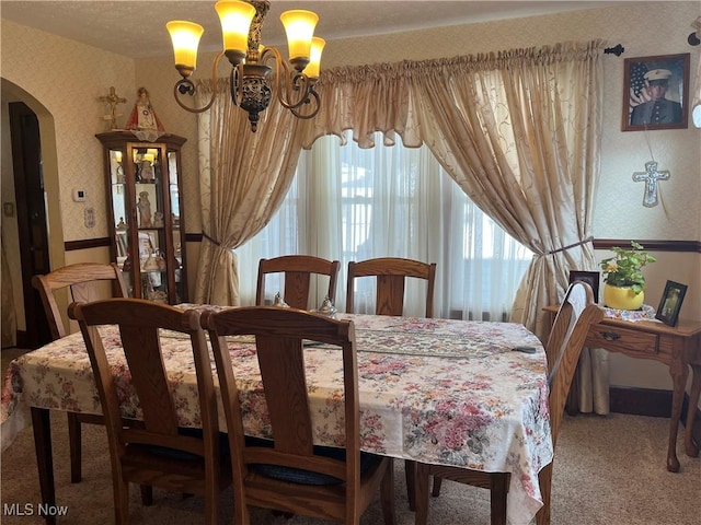 carpeted dining area with arched walkways, a notable chandelier, and wallpapered walls