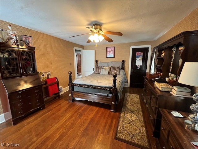 bedroom featuring dark wood-style floors, ceiling fan, a textured ceiling, baseboards, and wallpapered walls