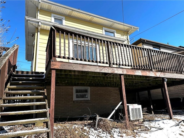 snow covered back of property featuring a wooden deck, stairway, central AC, and brick siding