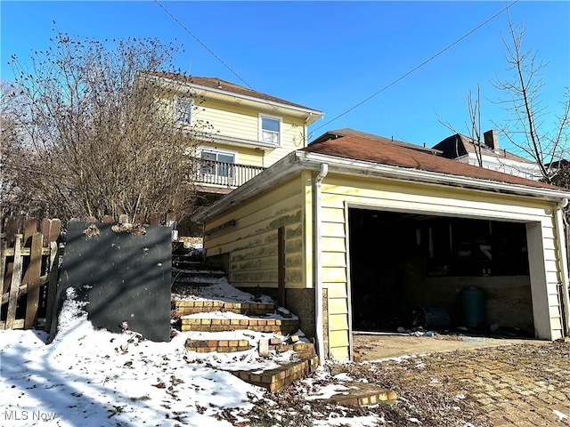 view of snowy exterior featuring a garage and fence