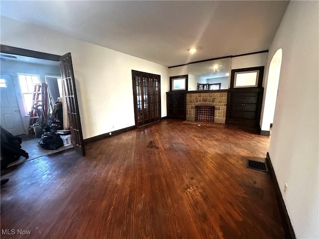 unfurnished living room featuring visible vents, dark wood finished floors, a stone fireplace, and baseboards