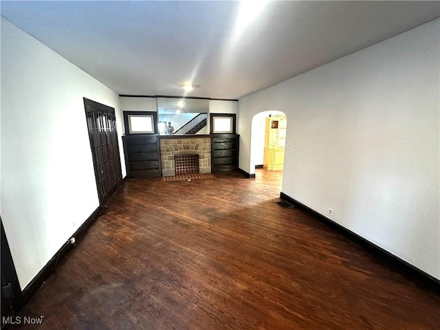 unfurnished living room with arched walkways, dark wood-style flooring, a fireplace, and visible vents