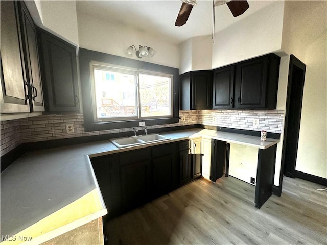 kitchen featuring tasteful backsplash, light wood-style flooring, a ceiling fan, a sink, and dark cabinets