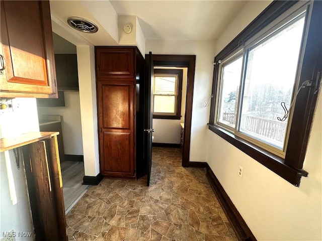 hallway with stone finish flooring, visible vents, and baseboards