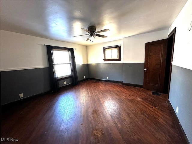 unfurnished room with baseboards, visible vents, dark wood finished floors, and a ceiling fan