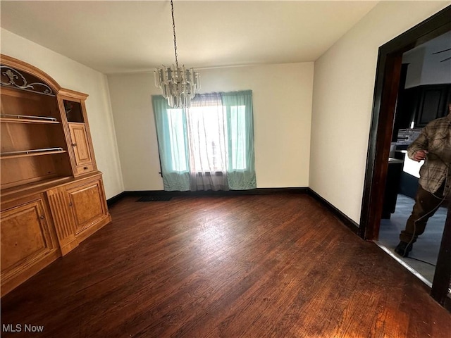 unfurnished dining area featuring baseboards, dark wood finished floors, and a notable chandelier