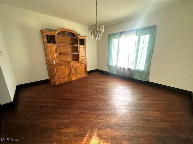 unfurnished dining area with dark wood-type flooring, a chandelier, and baseboards