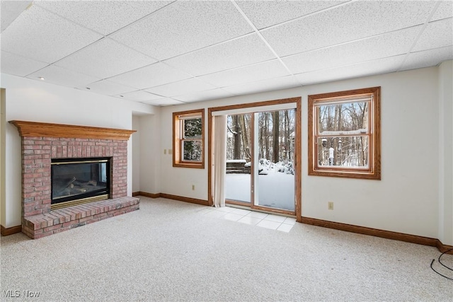 unfurnished living room featuring a paneled ceiling, a fireplace, baseboards, and light colored carpet