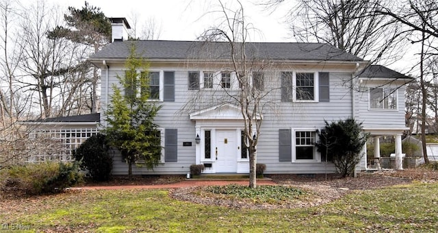 colonial house featuring a chimney and a front yard