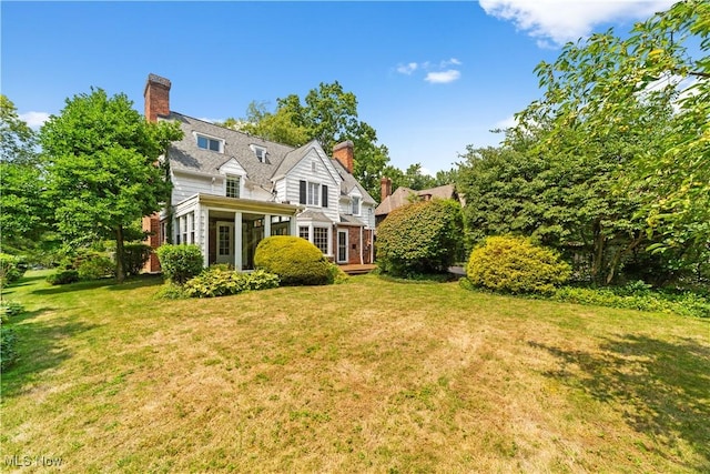 back of property featuring a yard, a chimney, and a sunroom