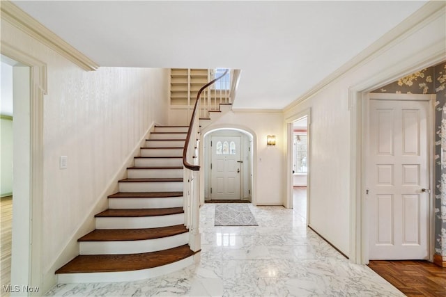 entryway with arched walkways, marble finish floor, crown molding, baseboards, and stairs