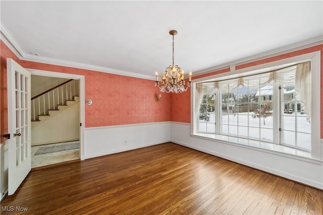 unfurnished dining area featuring a wainscoted wall, crown molding, wallpapered walls, and wood finished floors