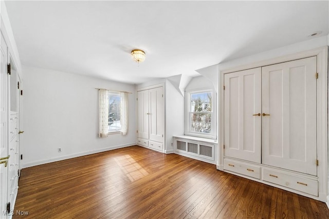 unfurnished bedroom featuring multiple closets, multiple windows, baseboards, and wood finished floors