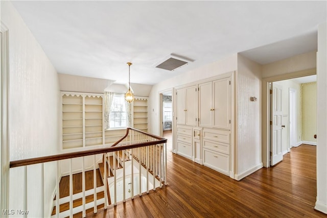 hall with dark wood-style floors, an upstairs landing, and baseboards