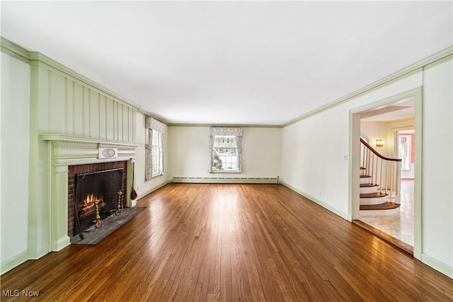 unfurnished living room with a fireplace, wood finished floors, stairs, baseboard heating, and crown molding